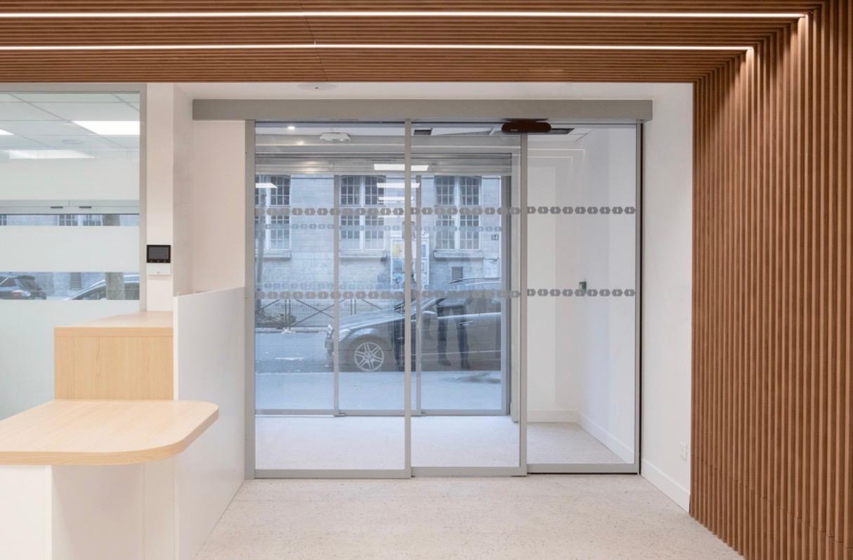 Hall d'accueil avec portes automatiques vitrées et habillage en tasseaux de bois