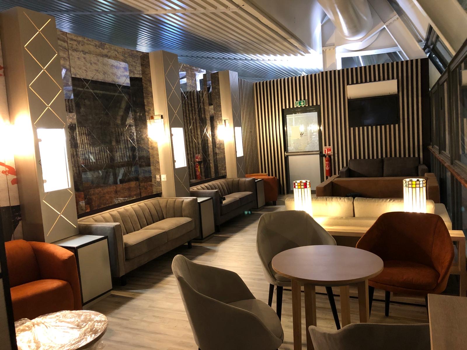 Salon lounge livré — banquettes, habillage miroir à croisillons dorés et éclairage d'ambiance