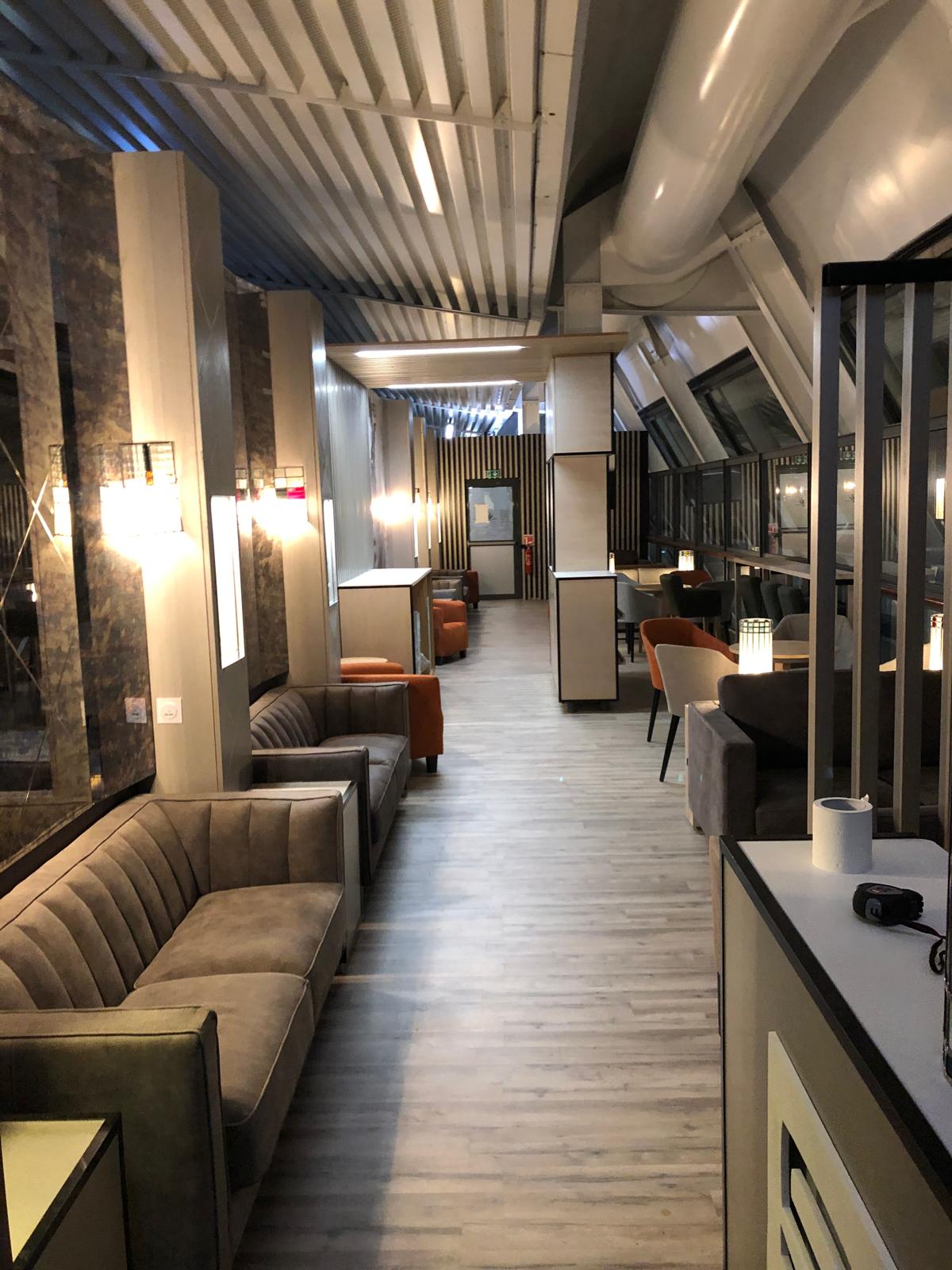 Allée du lounge — banquettes velours, appliques lumineuses et espaces salon en enfilade